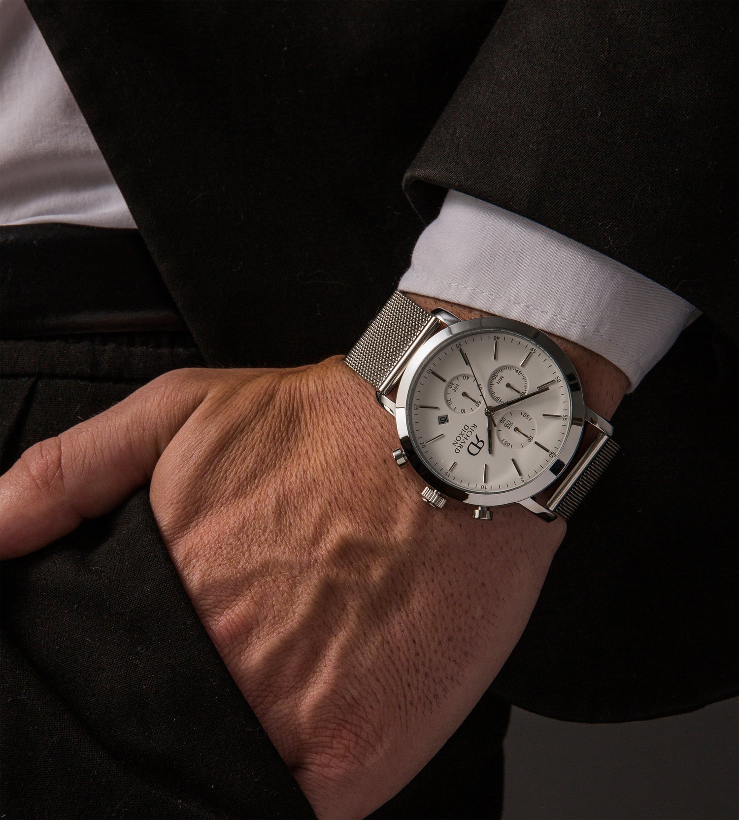 Relógio de homem Richard Dixon Iconic Chrono Mesh Silver White no pulso de um homem vestido de fato.